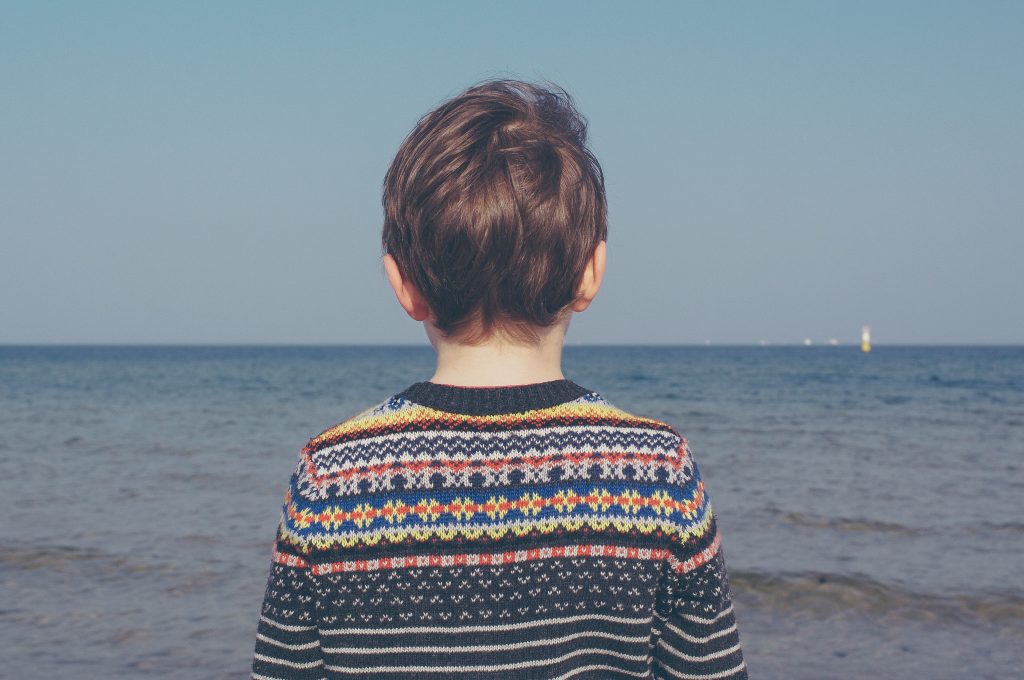 תמונה עצובה של ילד מסתכל על הים בסוודר צבעוני